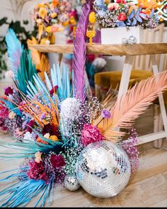 a disco ball surrounded by colorful flowers and feathers in front of a table with other decorations