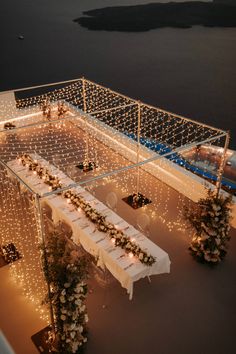 an aerial view of a table set up with lights and flowers on the tables in front of water