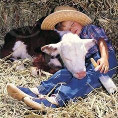 a young boy laying on the ground next to a cow with a straw hat on his head