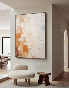 an abstract painting hangs on the wall next to a white chair and footstool