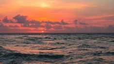 the sun is setting over the ocean with waves in front of it and some clouds