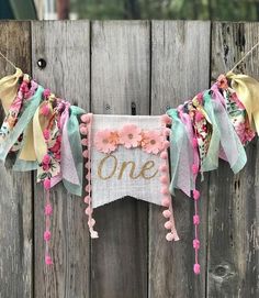 a one year old banner hanging on a fence with flowers and pom poms