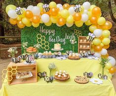 a table topped with lots of desserts and balloons in the shape of honeybees