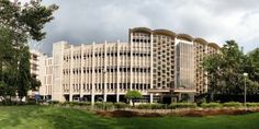 a large building sitting in the middle of a lush green park next to tall buildings