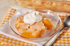 a glass bowl filled with fruit topped with whipped cream next to a fork and spoon