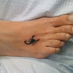 a small scorpion tattoo on the foot of a woman's left foot in black ink