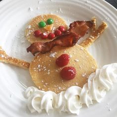 a white plate topped with pancakes covered in icing and toppings next to whipped cream