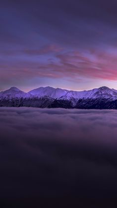 the sun is setting over some mountains covered in fog and clouds as seen from an airplane