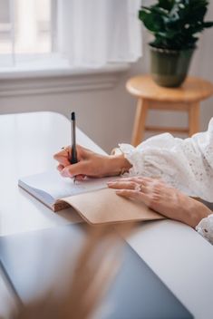 a woman sitting at a table with a notebook and pen in her hand, writing