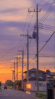 the sun is setting behind power lines and telephone poles in an area with houses on either side