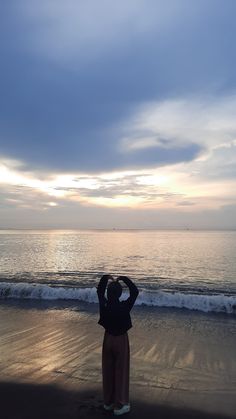 a person standing on the beach looking out at the ocean with their head in his hands