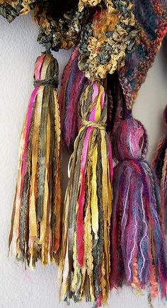 multicolored scarves hanging on the wall with tassels attached to them