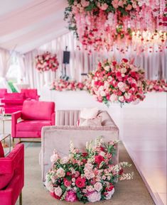 pink and white flowers are on display in front of couches, chairs and chandeliers