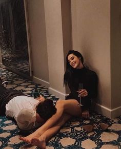 two women are sitting on the floor and one is holding a cell phone while the other holds a bottle