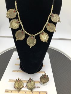 This complete vintage coin set includes a necklace, a pair of earrings, and a ring, is an epitome of tradition, as the design of the set is inspired by the Afghani Kuchi ornaments. The rusty gold toned set is embellished with dangling elements, adorned with intricate patterns and archaic motifs. The pair of earrings, coin shaped, complete the set in an astonishing manner, complimented by the antique ring in the identical design. You can pair this complete traditional set with any traditional or Metal Temple Jewelry In Round Shape, Vintage Gold Jewelry With Coin Pendant, Antique Metal Jewelry With Intricate Design, Festive Brass Temple Jewelry Sets, Gold Brass Coin Pendant Jewelry, Brass Coin Pendant Jewelry, Gold Coin Pendant Brass Jewelry, Gold Coin Shaped Metal Jewelry, Antique Gold Metal Jewelry