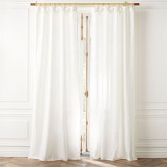 a white curtain hanging in front of a window with wood flooring and wooden floors