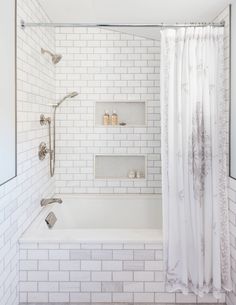 a white tiled bathroom with shower, tub and shelves on the wall next to it