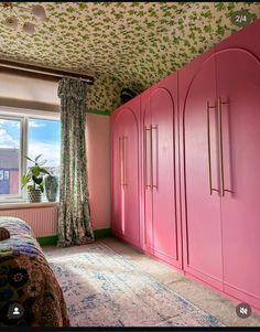 a bedroom with pink cabinets and floral wallpaper on the ceiling, along with a large window