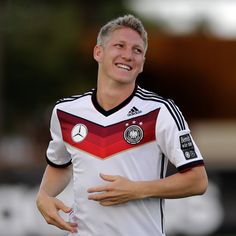 a soccer player is smiling and holding his hands out to the side while wearing a red, white and black uniform