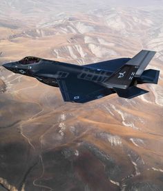 a fighter jet flying through the air over mountains and desert land in an aerial view