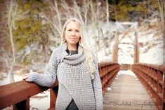 a woman is standing on a bridge in the snow wearing a gray sweater and scarf