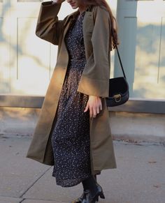 a woman in a dress and trench coat walking down the street with her hand on her head