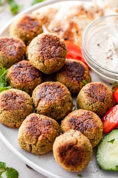 a white plate topped with meat patties and veggies next to a bowl of ranch dressing