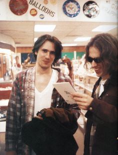 two young men standing next to each other in a store looking at something on a clipboard