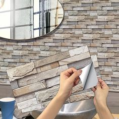 a person is holding a piece of paper in front of a brick wall with a mirror above it