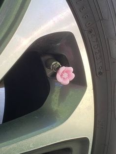 a pink flower sticking out of the side of a silver car door handle and tire