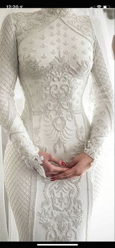 a woman in a white wedding dress with long sleeves and an intricate lace pattern on the skirt