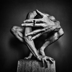 a black and white photo of a man's hands on top of a statue