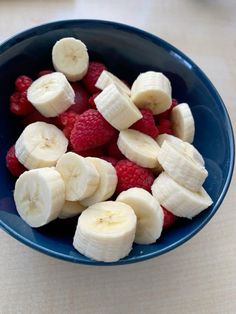 a blue bowl filled with bananas and raspberries