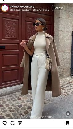 a woman standing in front of a red door wearing white pants and a trench coat