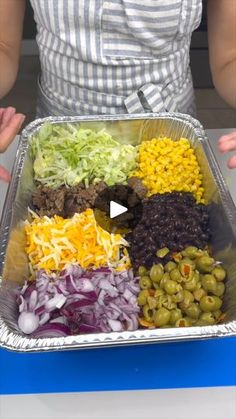 a person holding a tray with different types of food in it, including olives, onions, and beans