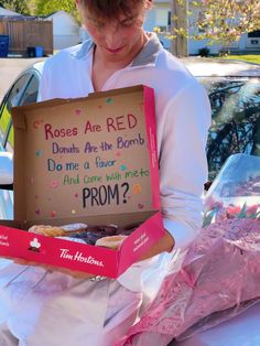 a woman holding a box with donuts in it that says roses are red do me at five and come with me from?