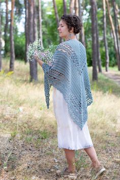 a woman is standing in the woods holding flowers and wearing a crocheted shawl