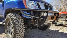 the front end of a blue truck parked on gravel