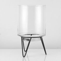 a glass vase sitting on top of a table next to a black metal stand with a white wall behind it