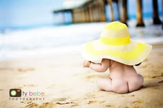 a baby sitting on the beach wearing a yellow hat