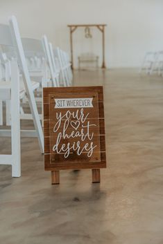 a wooden sign sitting in the middle of a room filled with white chairs and tables