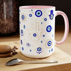 a pink and white coffee mug with an evil eye design on it next to a spoon