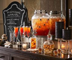 an assortment of halloween drinks on a buffet table with candles and candies in glass jars