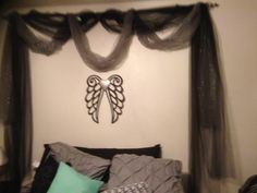 a bed with two pillows and some curtains on the headboard, along with an angel - shaped metal wall decoration