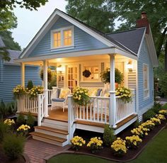 a small blue house with white porches and yellow flowers in the front garden area