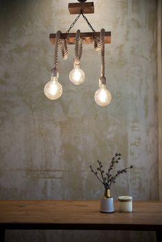 three light bulbs hanging from a wooden beam on a table next to a vase with flowers