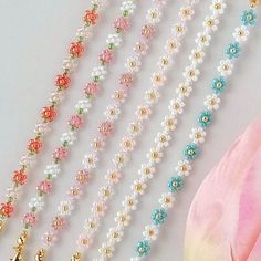 five strands of pearl beads with gold clasps and charms on white surface next to pink scarf