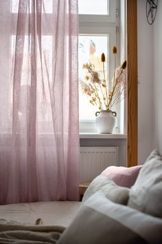 a window with pink sheer curtains in front of it and a vase filled with flowers