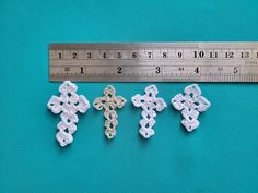 three crocheted crosses are next to a ruler on a blue surface, with one measuring the other