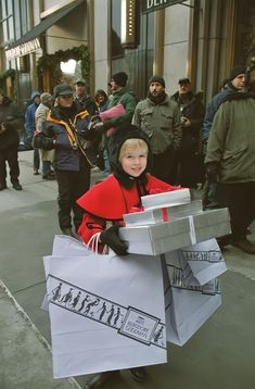 a young boy is carrying shopping bags on the street while people are standing around him